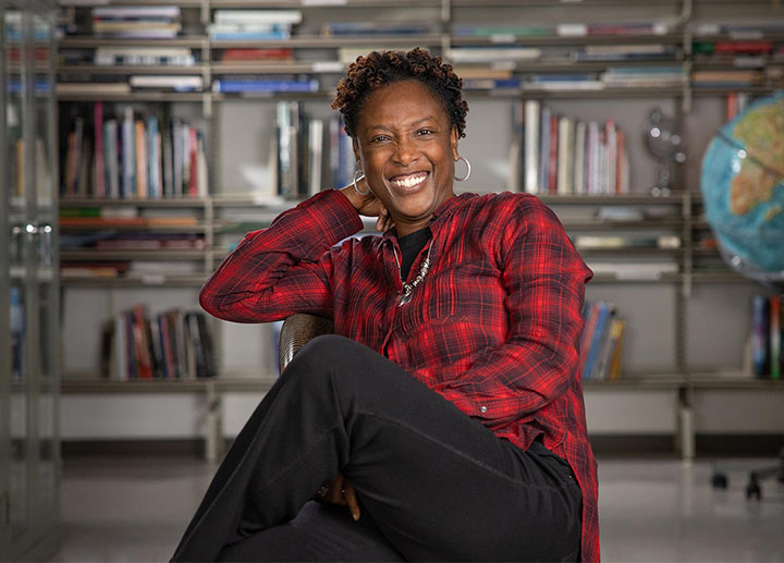 Female professor leaning back on a chair while smiling in front a bunch of books