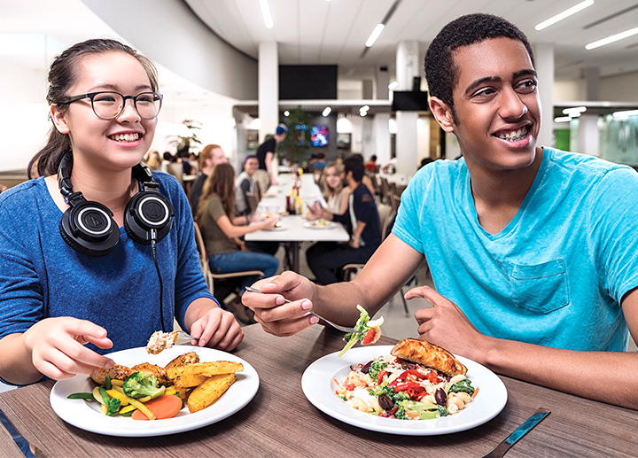 Two students eating food at a cafeteria and sitting together at a table 